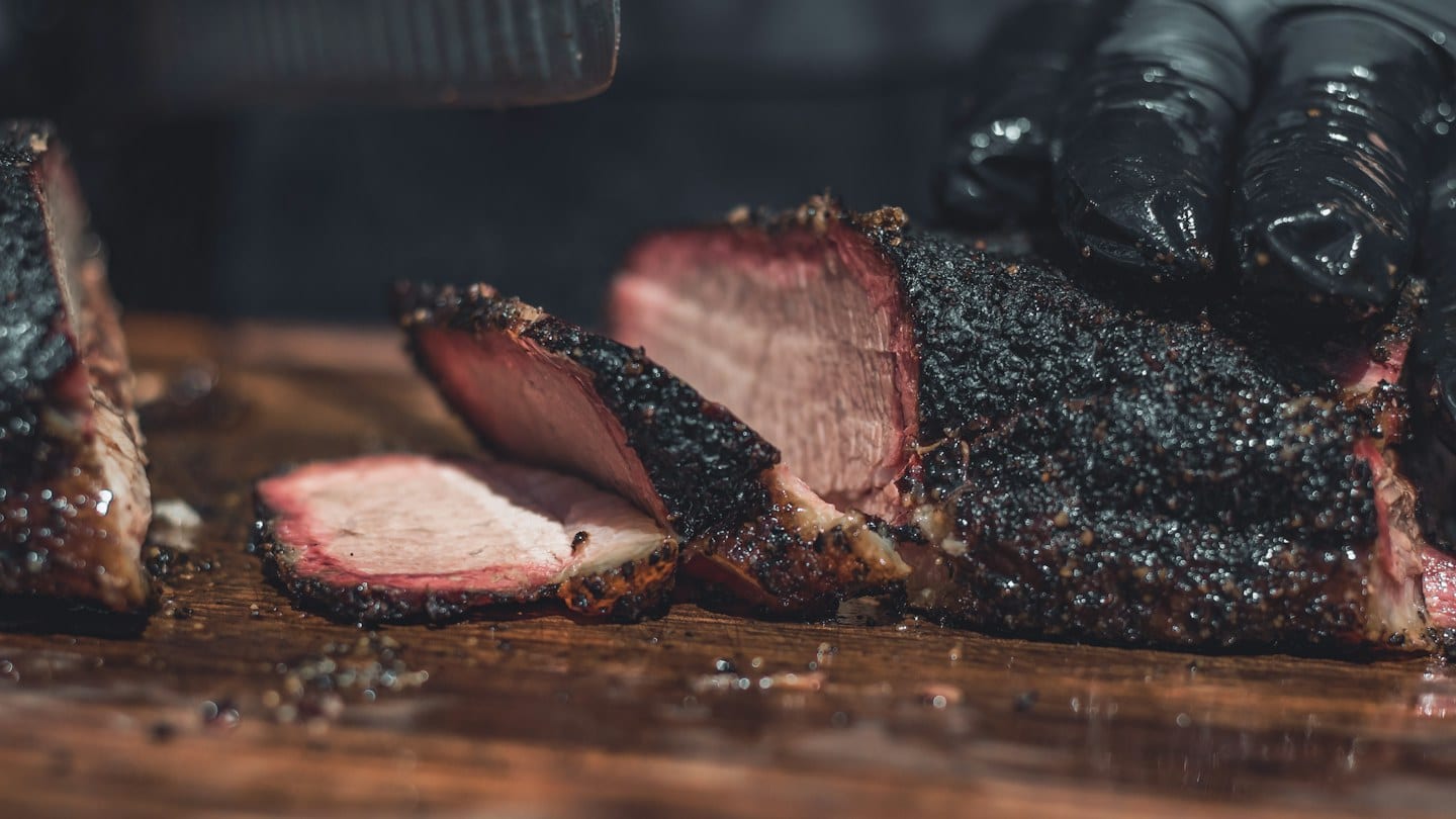 Sliced smoked meat on a wooden board; illustrative barbecue photography.